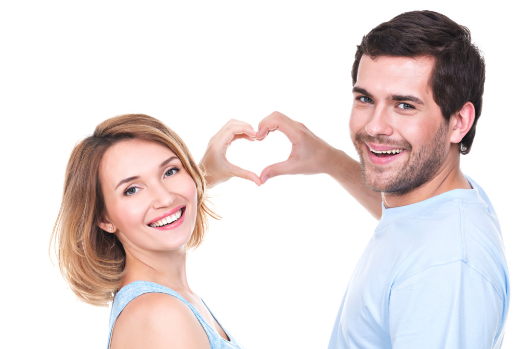 Portrait of cheerful smiling couple standing together show hands heart -  isolated on white background.